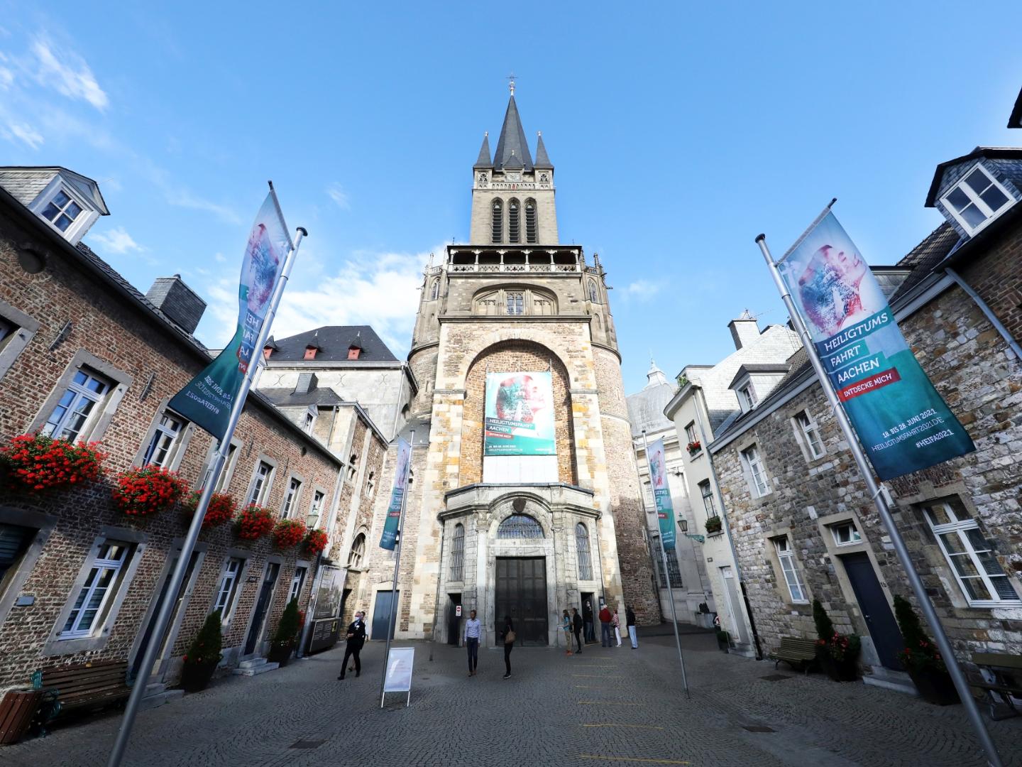Rund um den Aachener Dom erstrahlt nicht nur auf zahlreichen Fahnen das Grün der Heiligtumsfahrt: Über dem Hauptportal des Doms weist ein Großtransparent auf die Wallfahrt hin, die vom 18. bis 28. Juni 2021 stattfindet.
